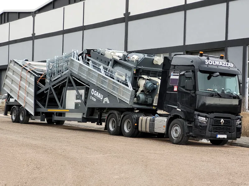 Centrale à béton mobile GRAU G100M repliée pour le transport et attelée à un tracteur routier noir près de l’usine