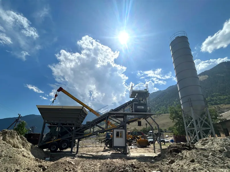 GRAU mobile concrete plant being installed in a sunny mountain valley, with a single silo and a yellow crane boom