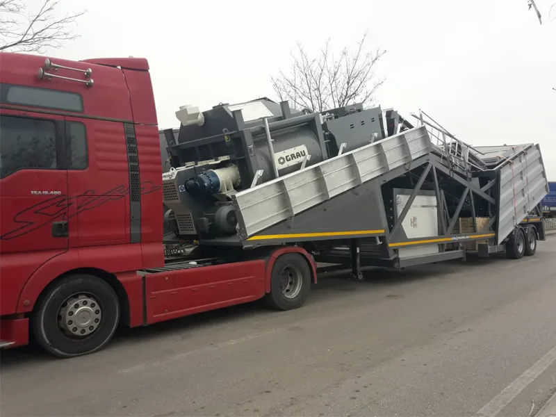 Planta de hormigón móvil GRAU G100M plegada para el transporte y enganchada a una cabeza tractora roja